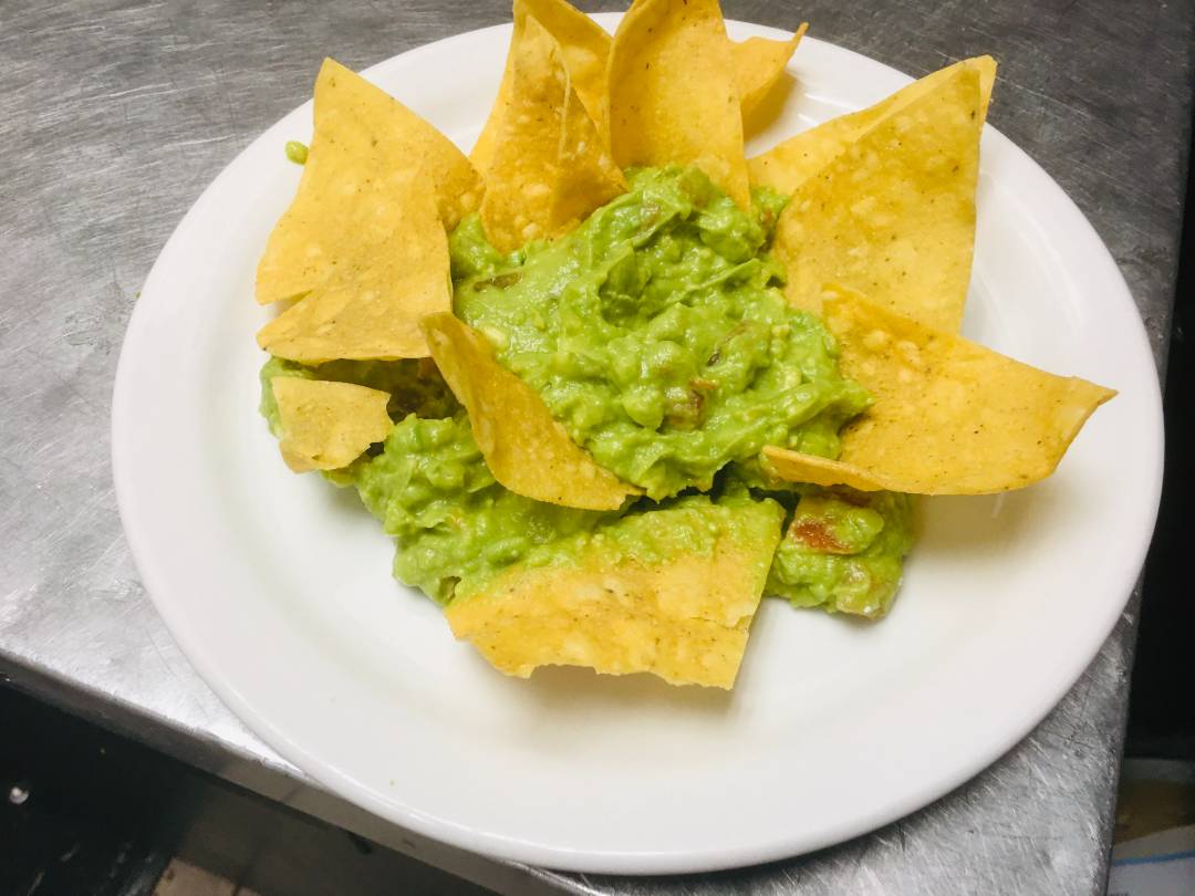 Guacamole on a white plate decorated with tortilla chips.