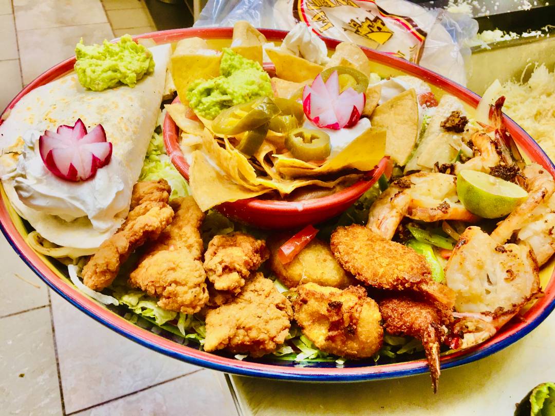A plate featuring chicken, nachos with guacamole and various vegetables.
