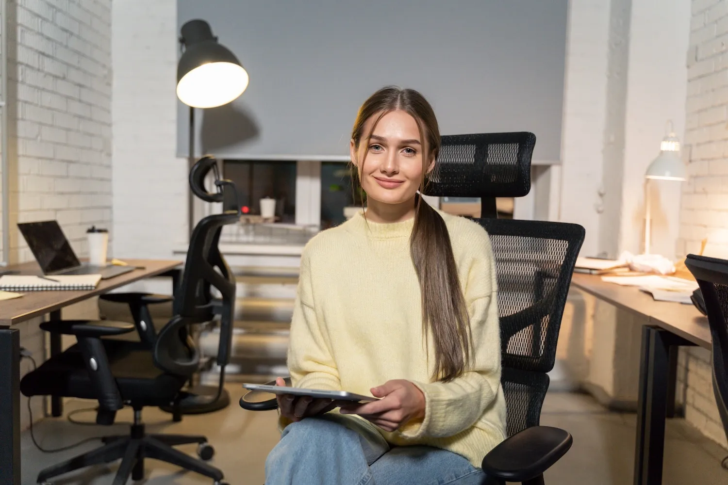 Woman in yellow sweater working at desk with tablet in modern office