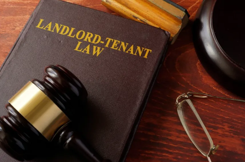 A brown leather-bound book titled "LANDLORD-TENANT LAW" resting on a wooden desk next to a judge's gavel and a pair of reading glasses.