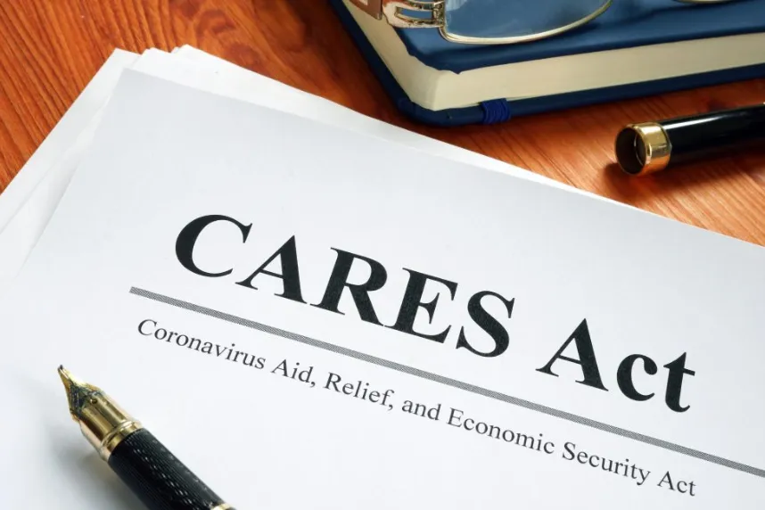 A formal legal document titled "CARES Act" and "Coronavirus Aid, Relief, and Economic Security Act" resting on a wooden desk next to a gold fountain pen and blue glasses case.