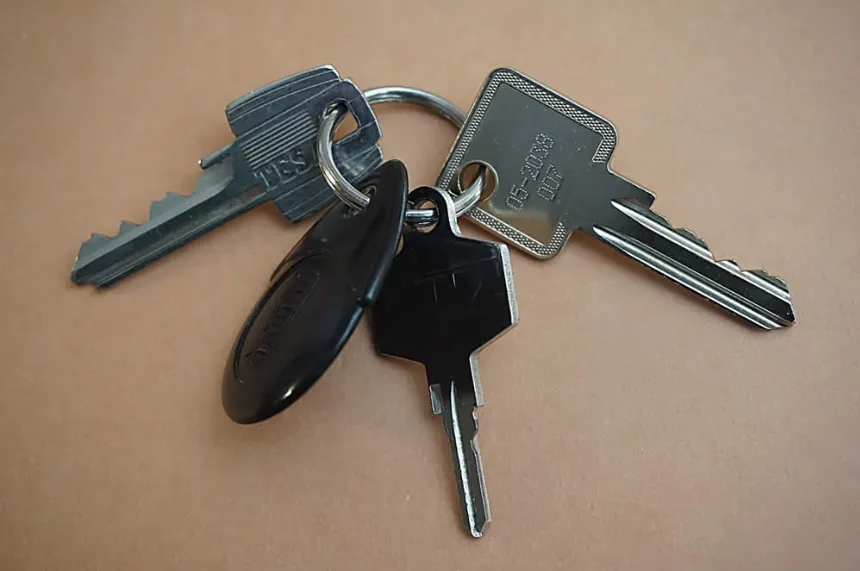 A bunch of metal house keys and a black plastic fob on a silver key ring, laying on a neutral tan surface.
