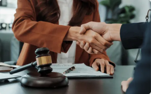Close-up of a handshake over a legal contract and judge's gavel symbolizing a successful legal settlement.