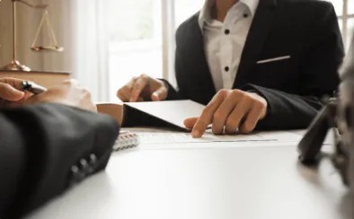 A professional man in a dark suit sitting at a desk and reviewing a legal document, with a judge's gavel and gold scales of justice visible in the foreground.