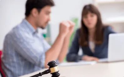 A blurred background of a man and woman in a meeting with a wooden judge's gavel in sharp focus in the foreground, representing litigation and dispute resolution services.