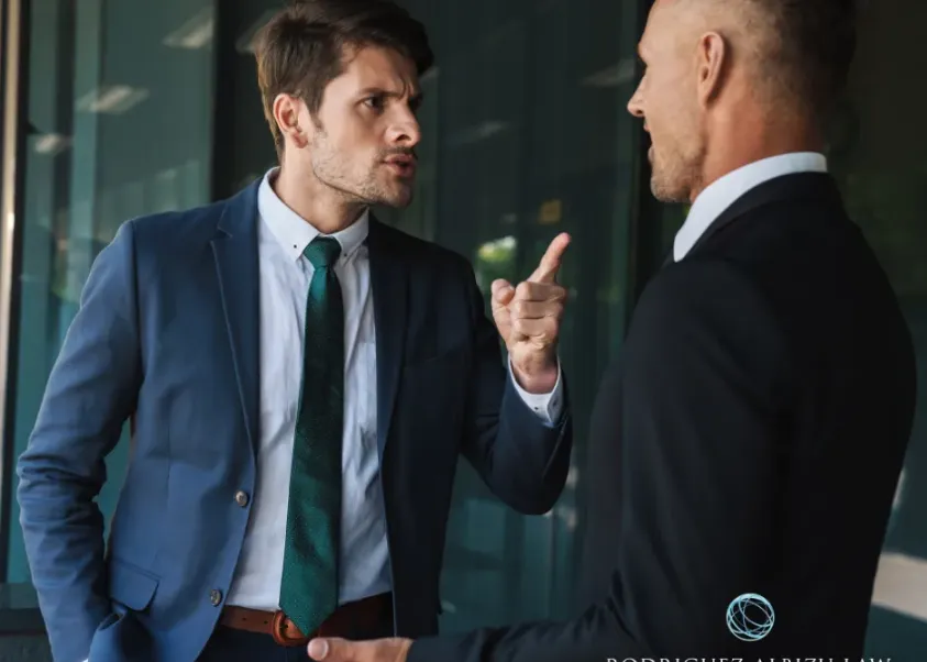 Two businessmen in suits engaged in a heated discussion or confrontation in a modern glass office, highlighting the need for aggressive legal representation.