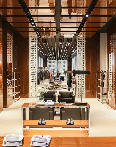 Modern retail store interior with wooden and mirrored décor, displaying shoes, clothes, and accessories on shelves and racks.