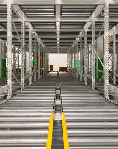 Empty industrial metal conveyor rollers aligned in a symmetrical warehouse aisle with stacked pallets visible at the far end.