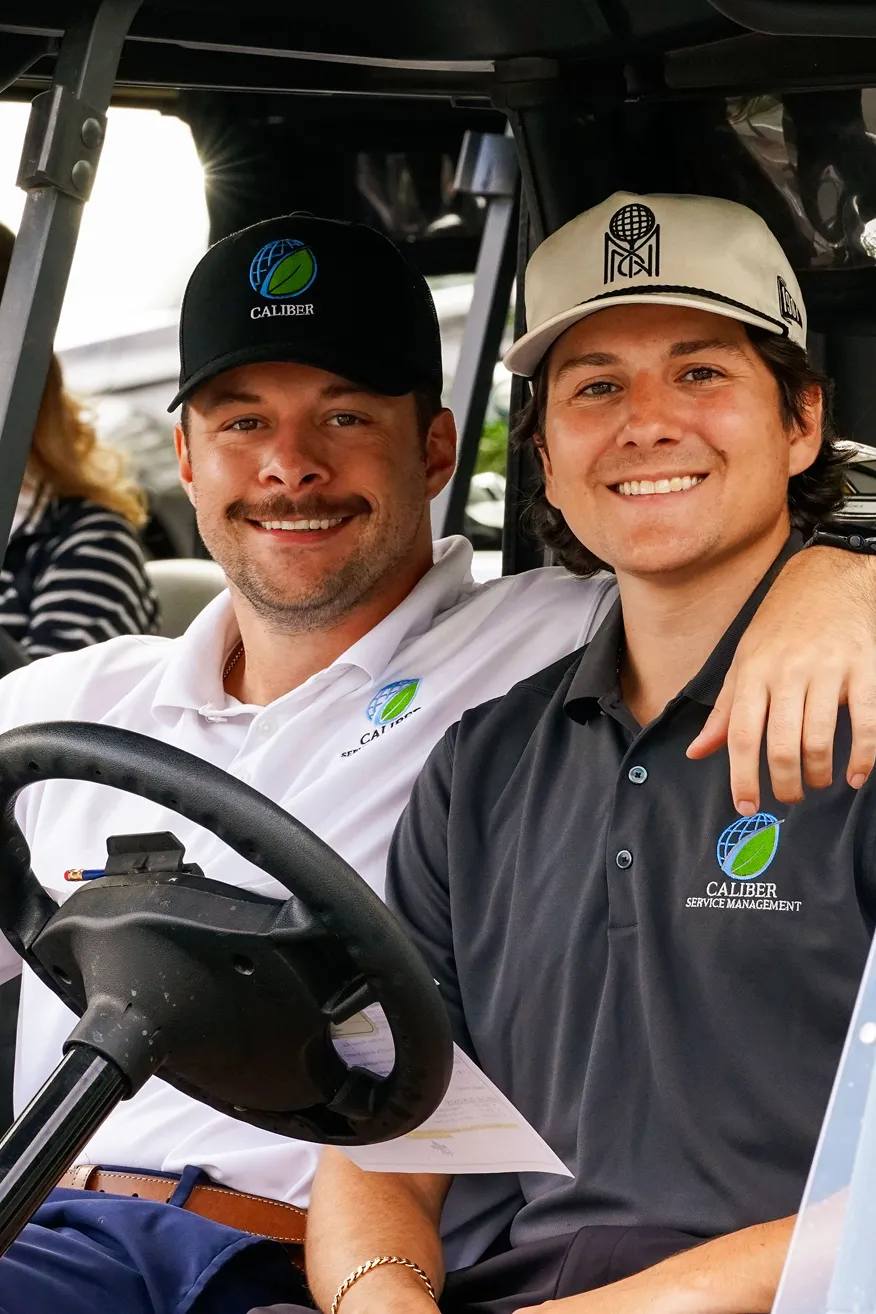 Three people wearing safety glasses and yellow lanyards, standing in front of an open electrical control panel.