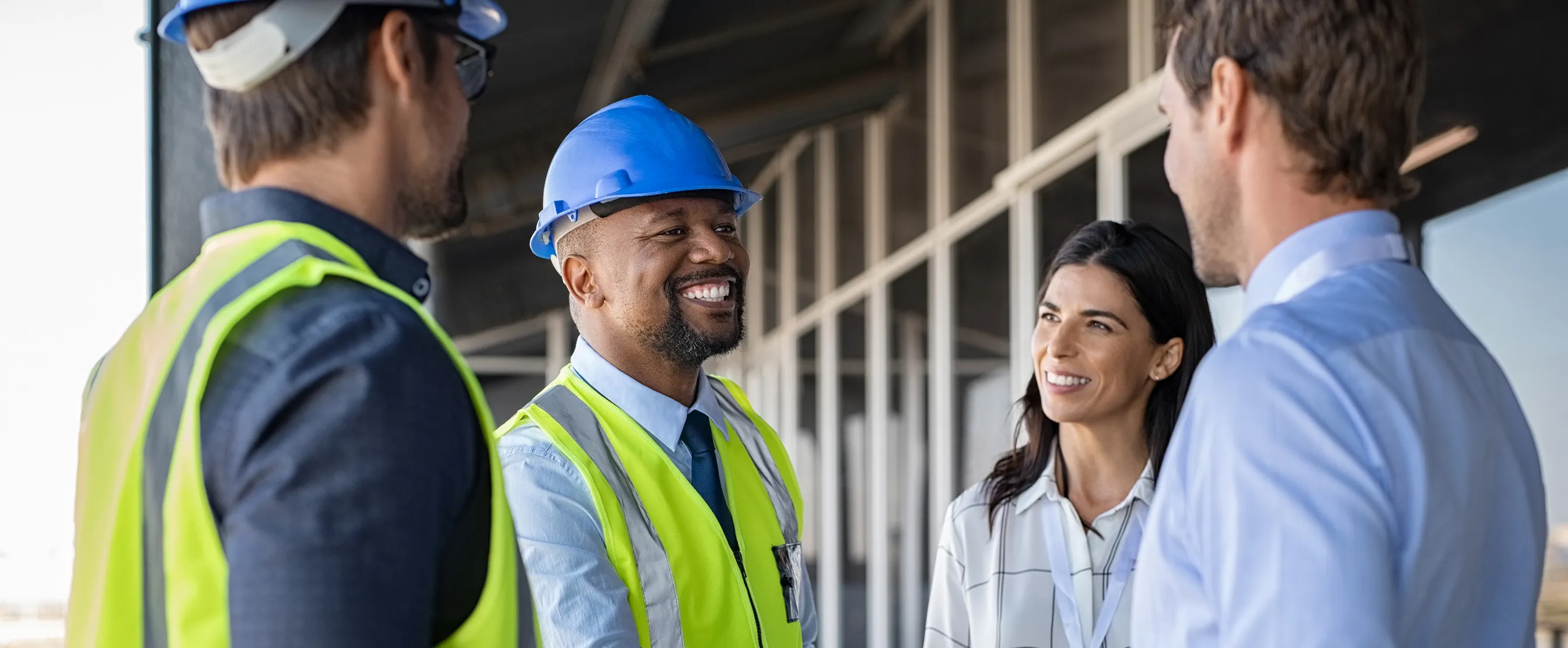 Two men in safety vests and hard hats smiling and shaking hands with a woman and another man in business attire at a construction site.