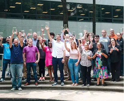 Group of diverse people standing on steps outdoors, smiling and raising clear glass awards in celebration.