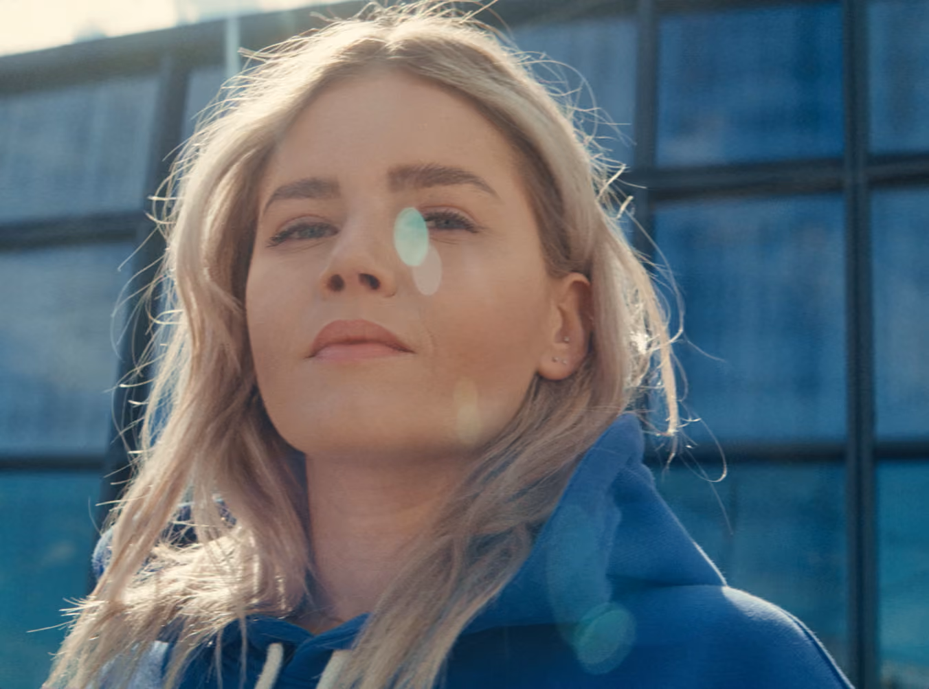 Portrait of a woman outside a glass-fronted building, with sunlight across the frame.