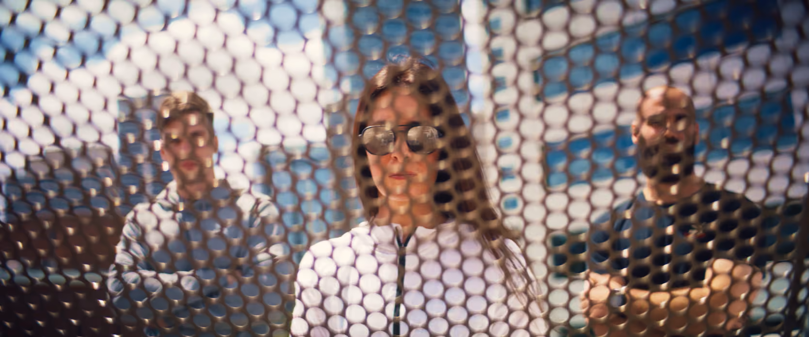 Three people seen through a perforated metal screen outside a building.