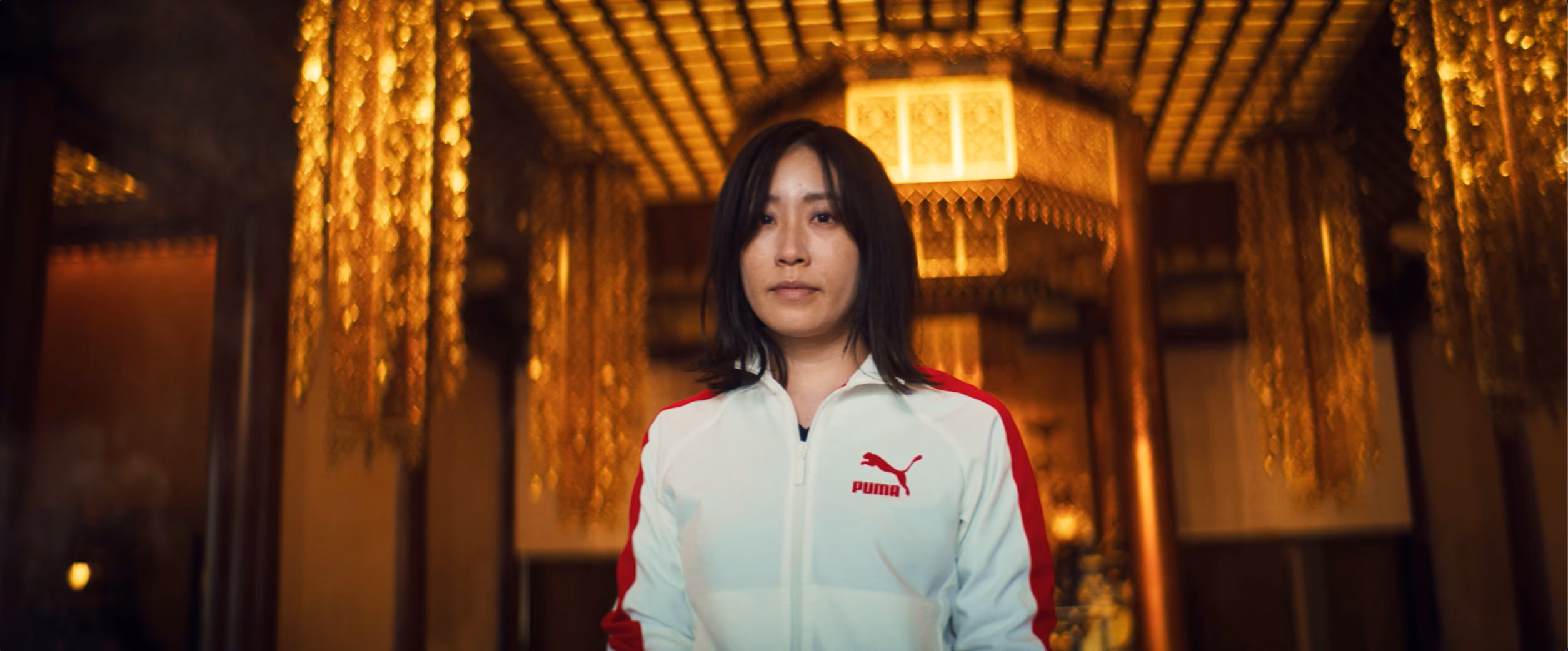 Portrait of a woman in a white PUMA jacket in a gold-lit interior.