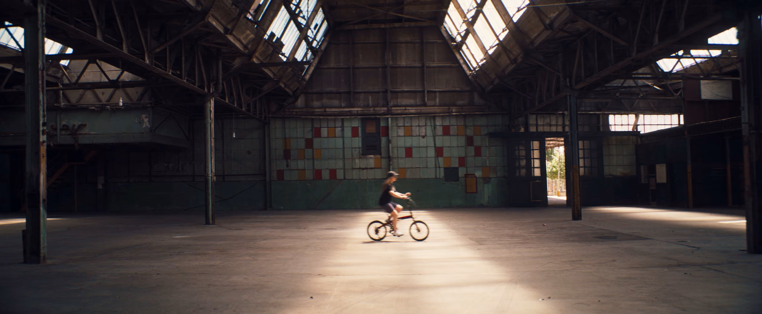 A cyclist rides through a large industrial hall beneath roof windows.