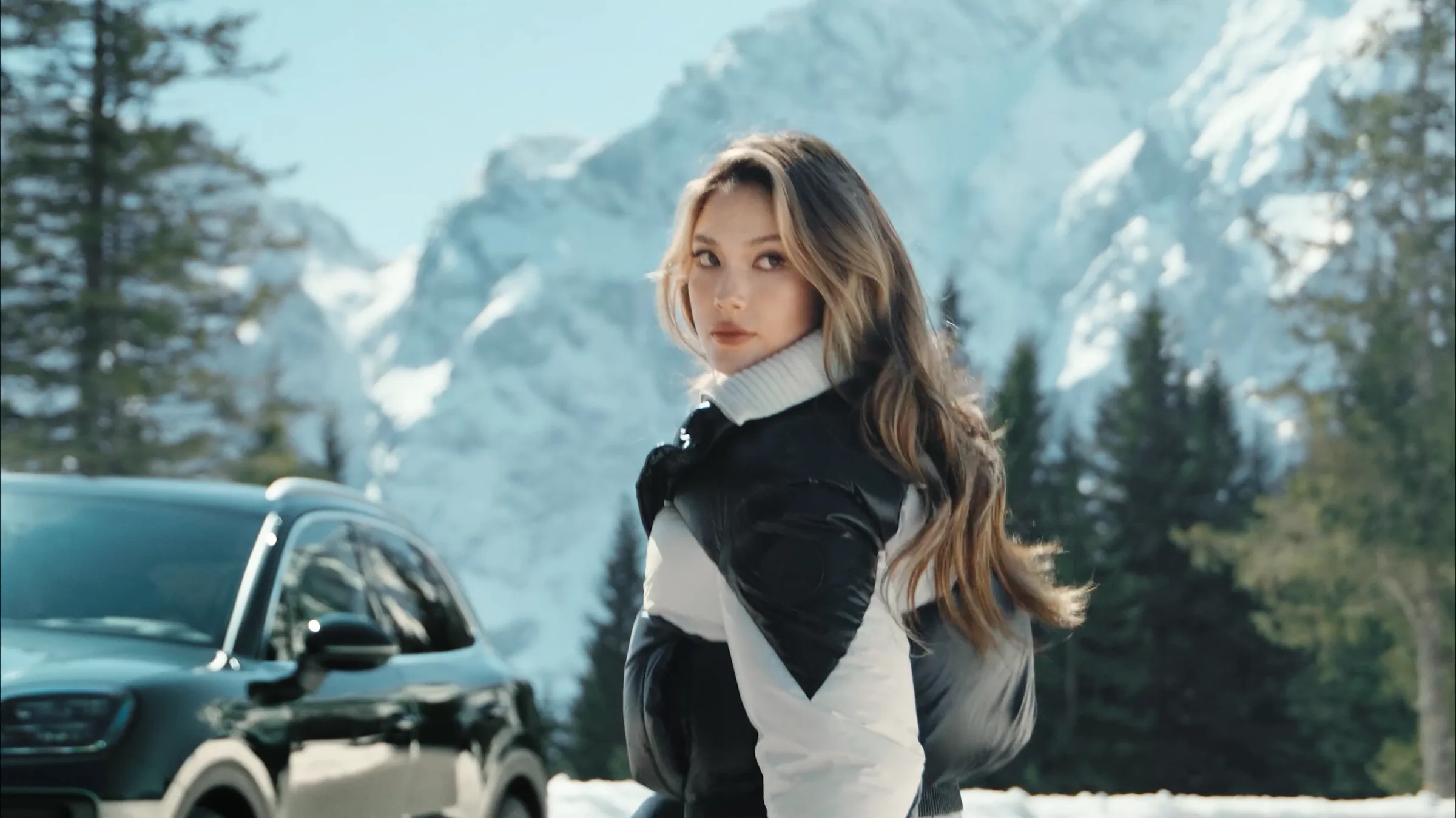Eileen Gu standing beside the Porsche Cayenne Active in the snow covered Berchtesgaden Alps, film still by IVORY Productions