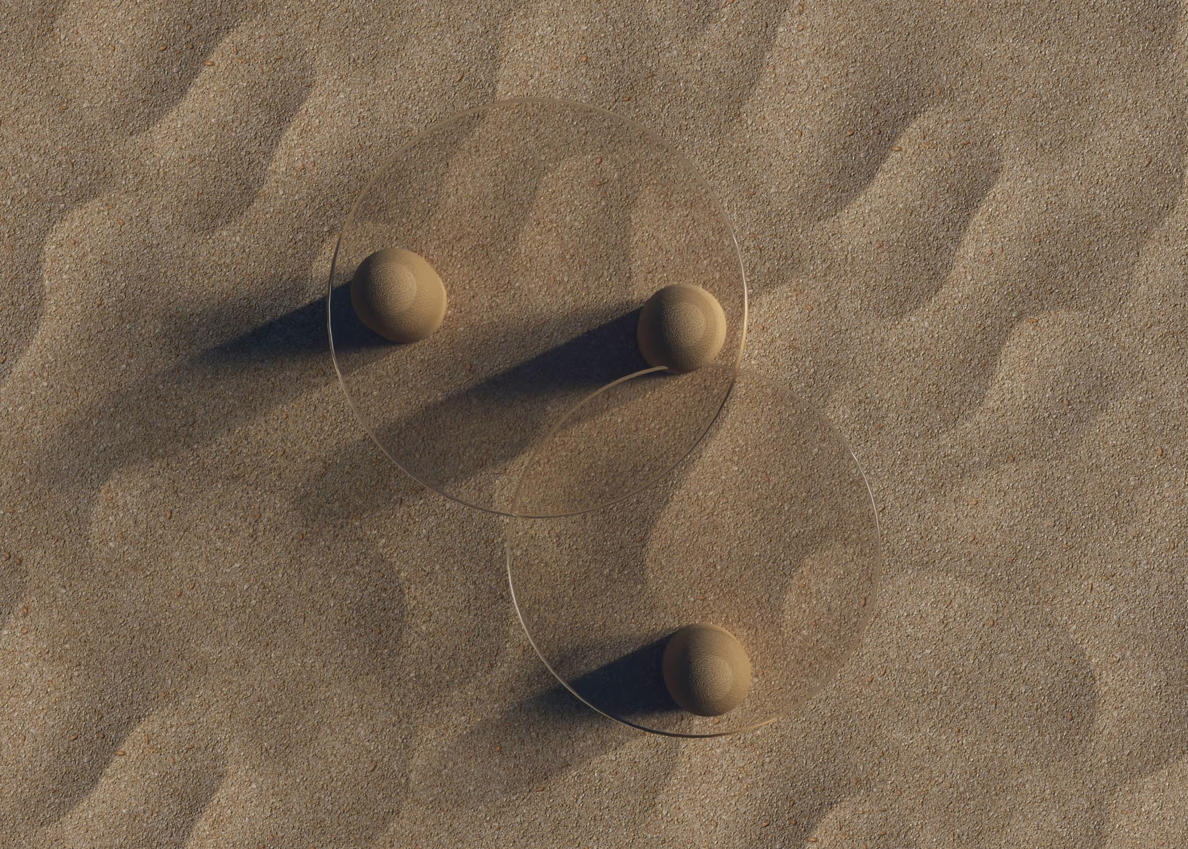 Deux cercles transparents posés sur du sable avec trois petites boules de sable créant des ombres allongées.