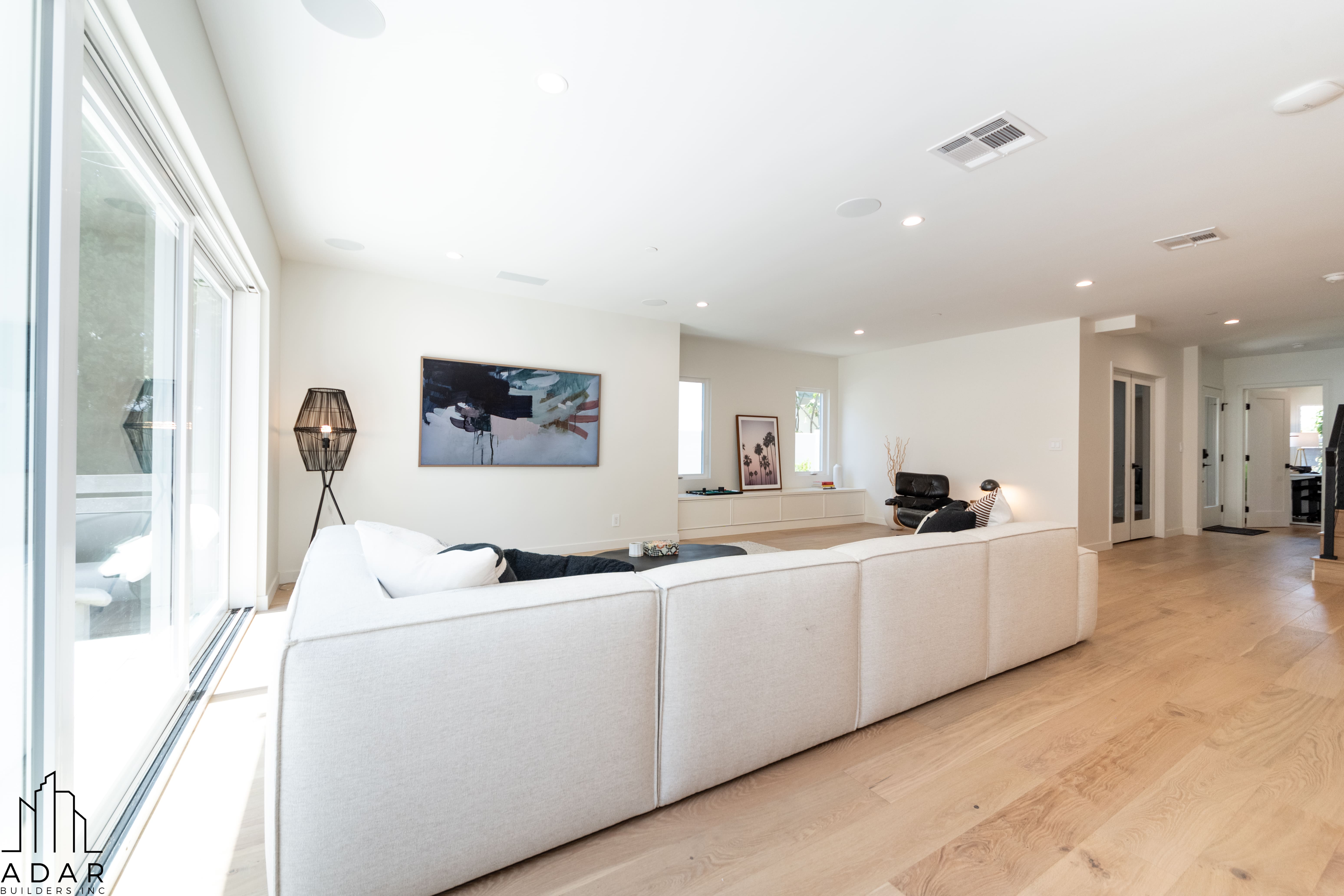 Bright modern living room with a large white sectional sofa, wooden floor, abstract wall art, and large sliding glass doors.
