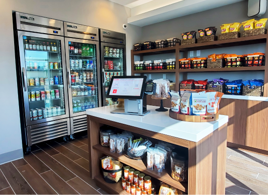 Fully stocked hotel lobby market with branded shelving, refrigerated drinks, and snacks for self-checkout.