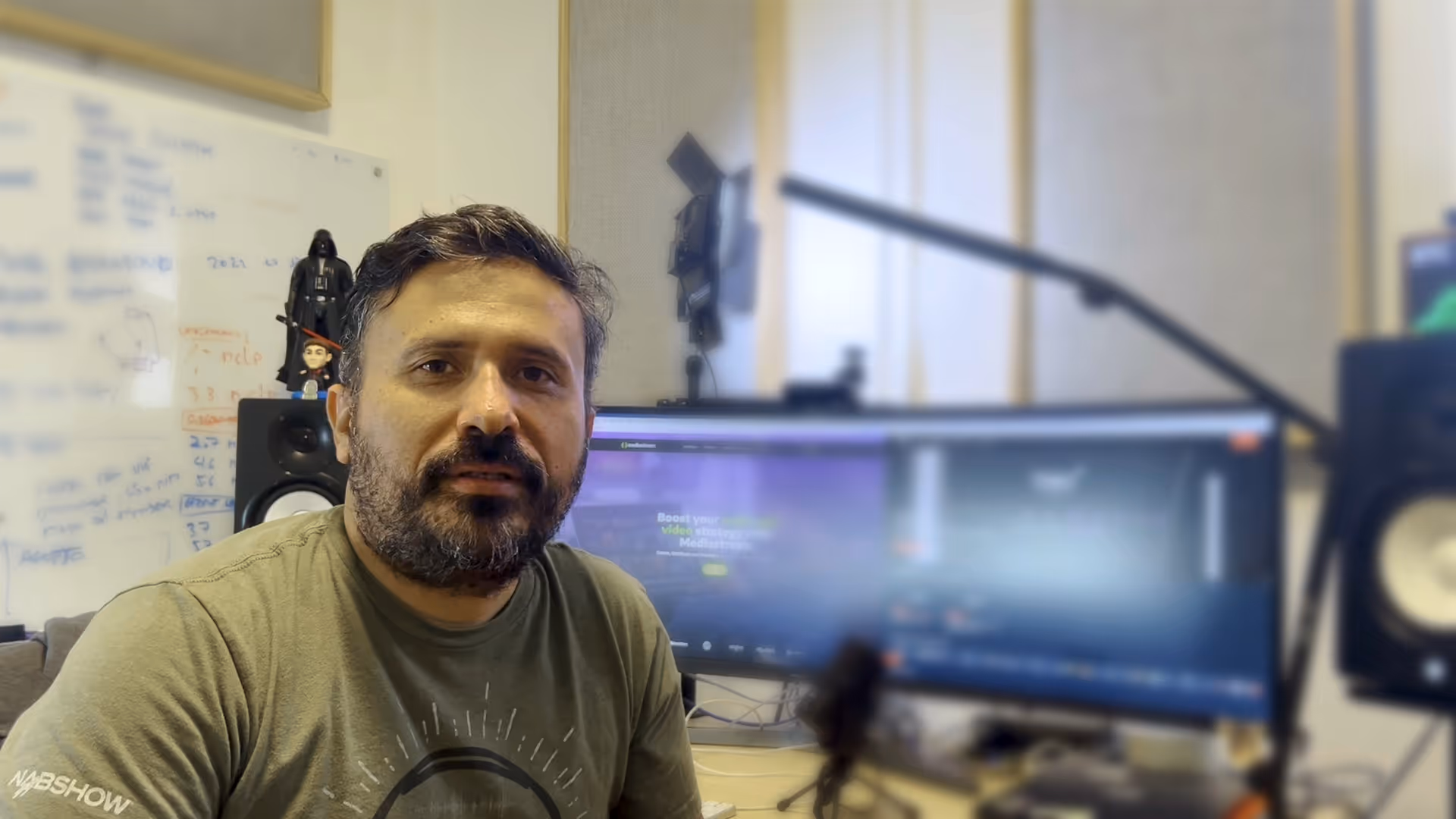 A man with a beard and mustache is sitting in front of a computer screen.