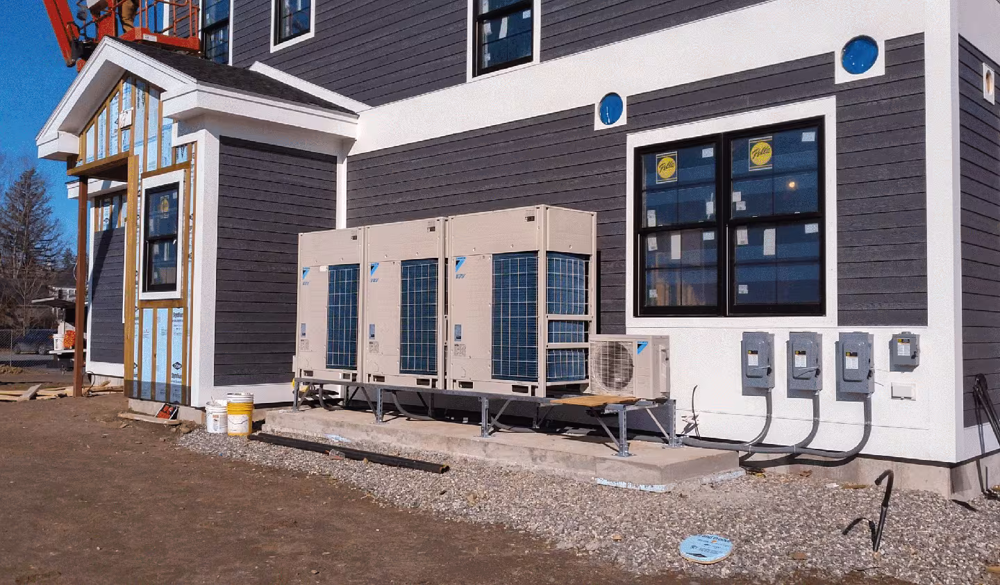 Commercial HVAC units installed outside a building under construction, with electrical panels and siding work in progress.