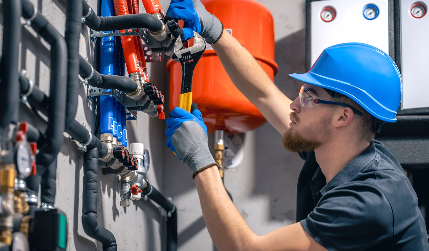 Plumber installing heating system in residential home, inspecting pipes with wrench.