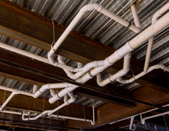 Plumbing rough-in stage in a commercial building under construction, featuring exposed white PVC pipes on a concrete ceiling