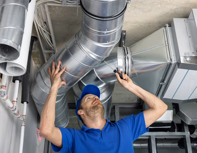 HVAC technician installing ducted piping, wearing work uniform and tools.