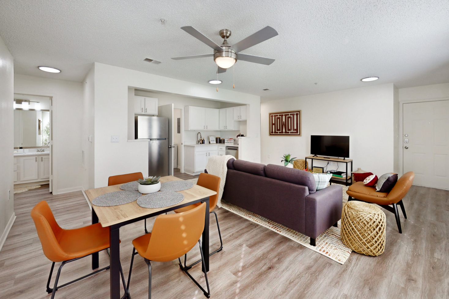 A wide view of a furnished apartment dining area with table and chairs and view of common area with a sofa on a white rug