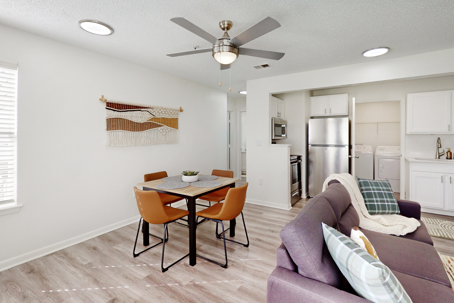 A wide view of a furnished apartment dining area with table and chairs and view of common area with a sofa 