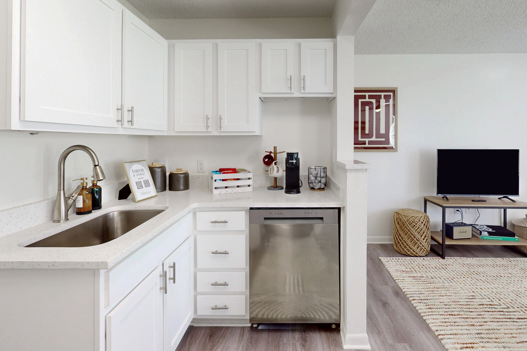 kitchen with stainless steel dishwasher, sink, white cabinets, and view of living area tv