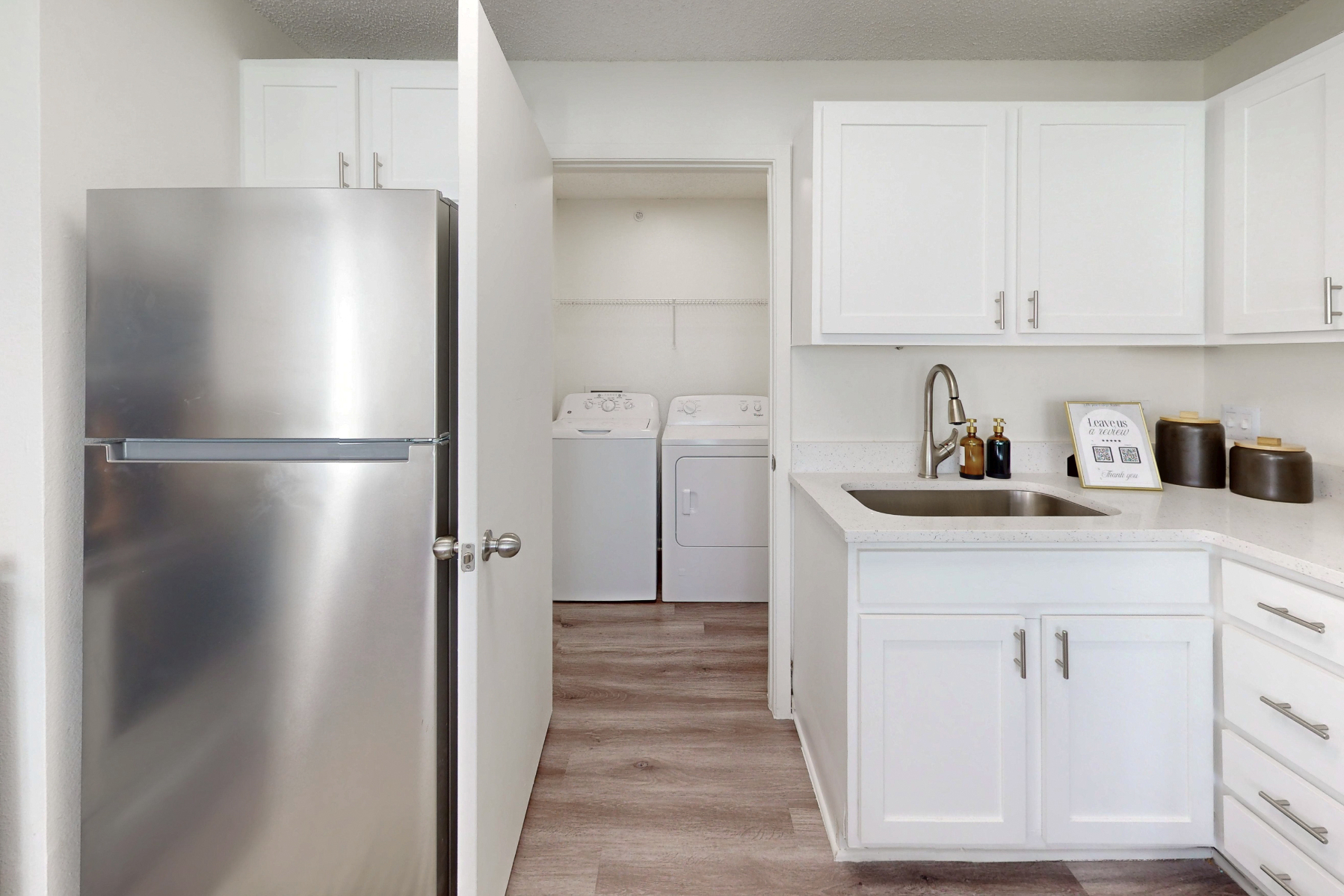 kitchen with stainless steel refrigerator, white cabinets, and view of laundry room with white appliances
