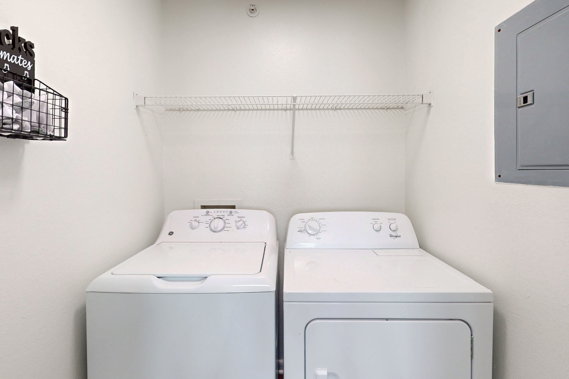 A dedicated laundry closet with a side-by-side white washer and dryer unit, featuring a wire shelf above for storage.