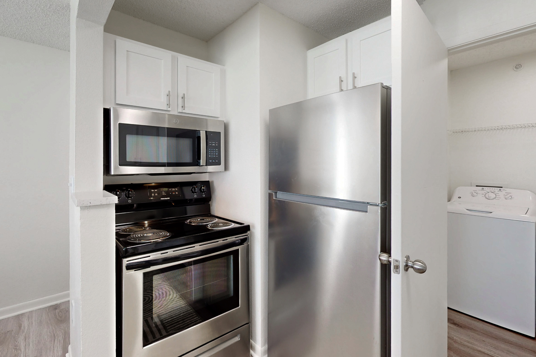 kitchen with stainless steel refrigerator, over, and microwave and view of laundry room with white appliances and shelf