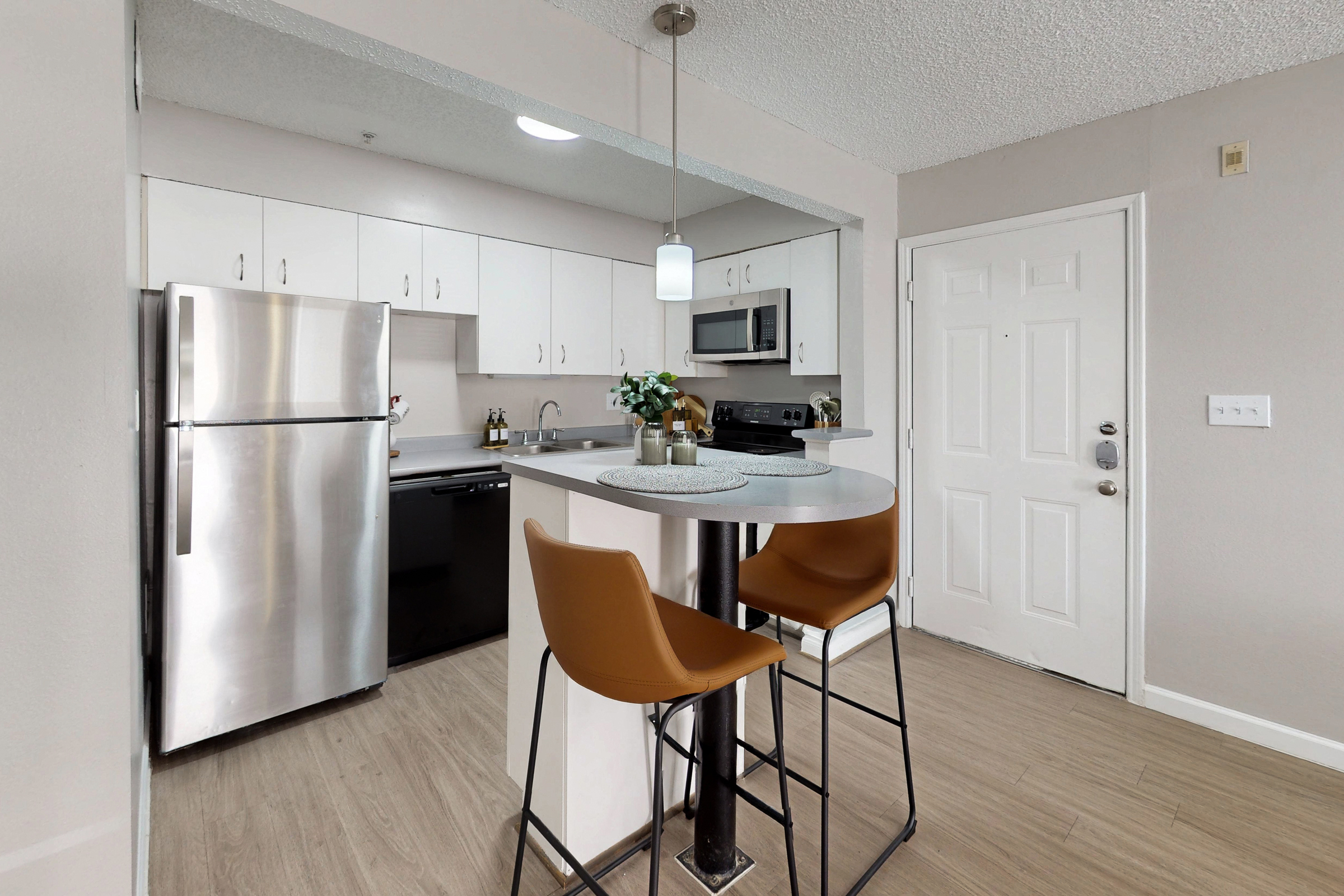 A wide view of a furnished apartment dining area with table and chairs and view of common area with a sofa on a white rug