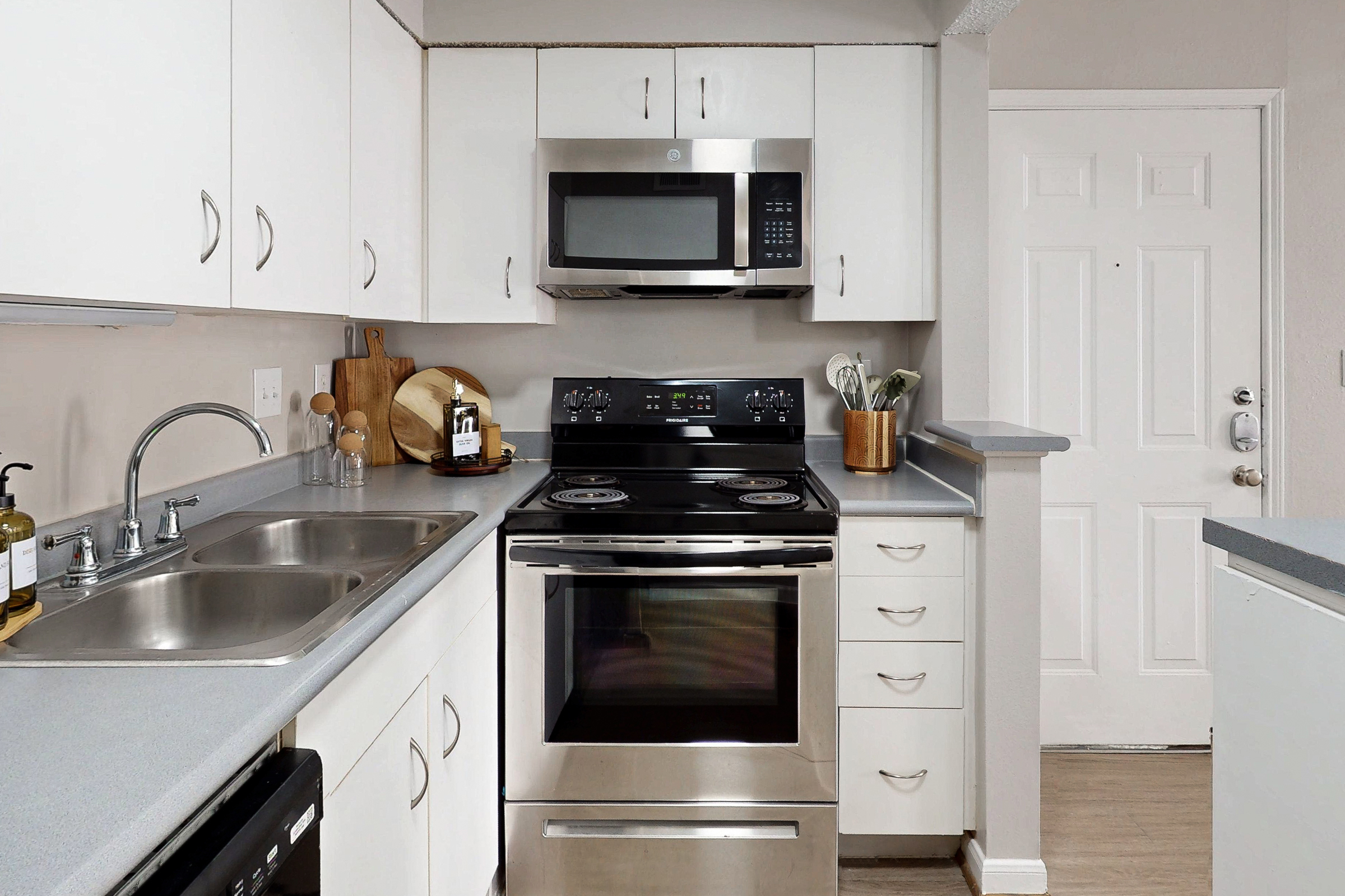 A wide view of a furnished apartment common area with a sofa and armchair on a white rug, coffee table and tv