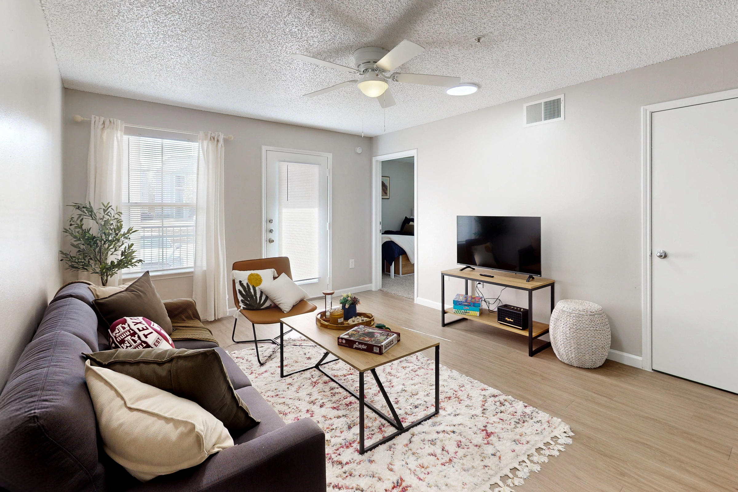 A wide view of a furnished apartment dining area with table and chairs and view of common area with a sofa on a white rug