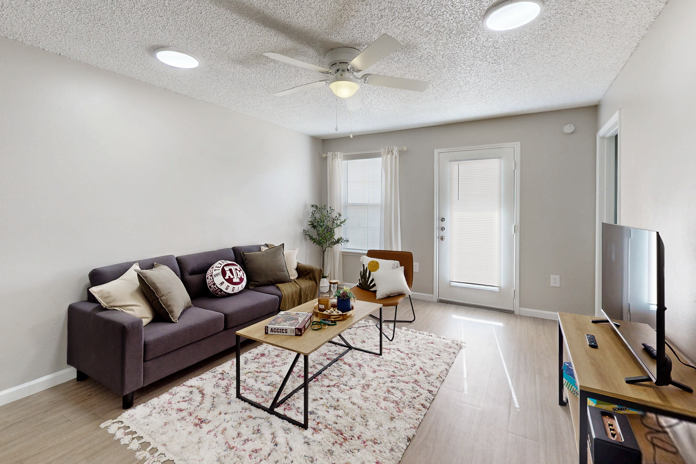 kitchen with stainless steel dishwasher, sink, white cabinets, and view of living area tv