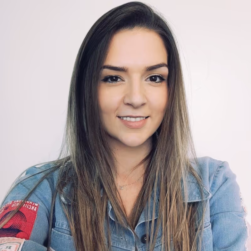 Smiling young woman with long straight hair wearing a denim jacket with patches on the left sleeve.