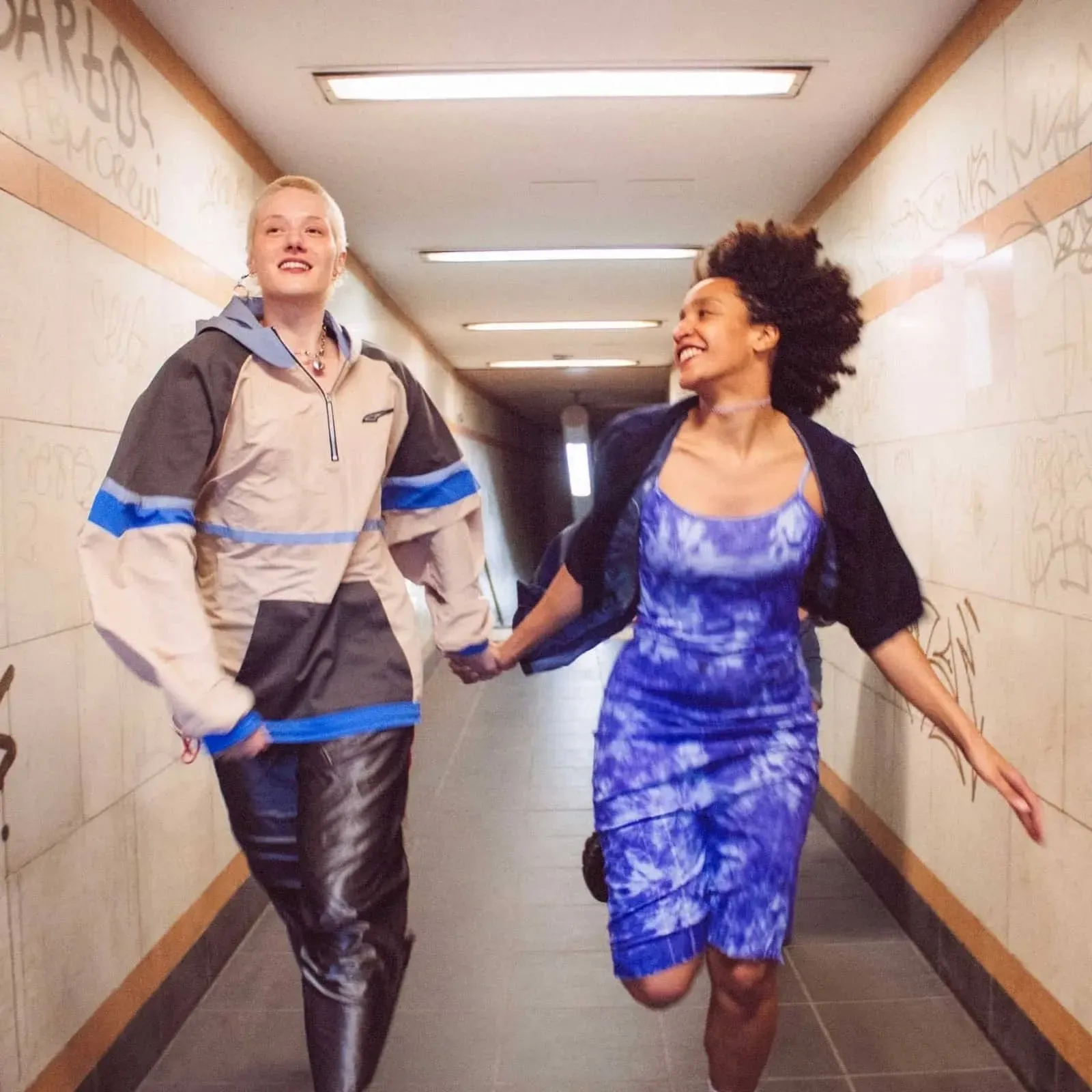 Two people hold hands and run down a hallway, grinning