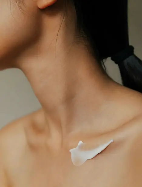 Close-up of a woman's neck and shoulder with a dollop of white cream on her collarbone.