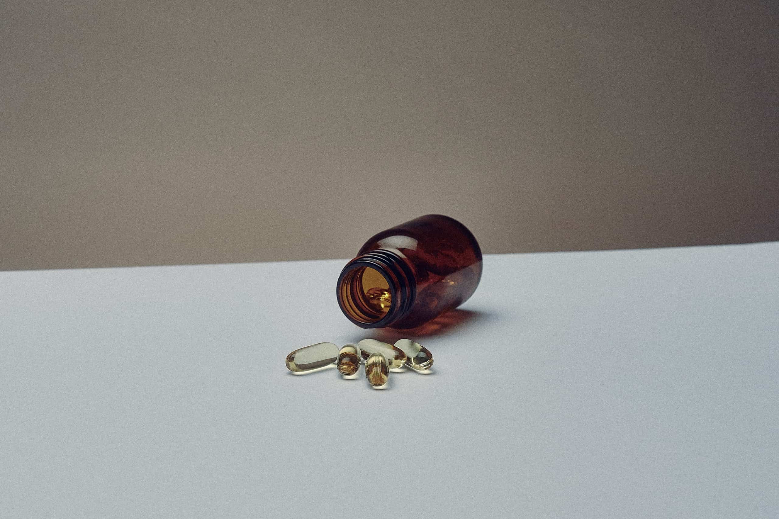 Amber glass bottle on its side with spilled translucent golden-yellow gel capsules representing supplements or probiotics.