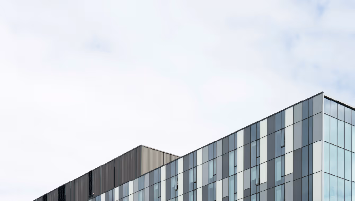 Modern glass office building under a cloudy sky, representing Tenet’s commercial real estate services.