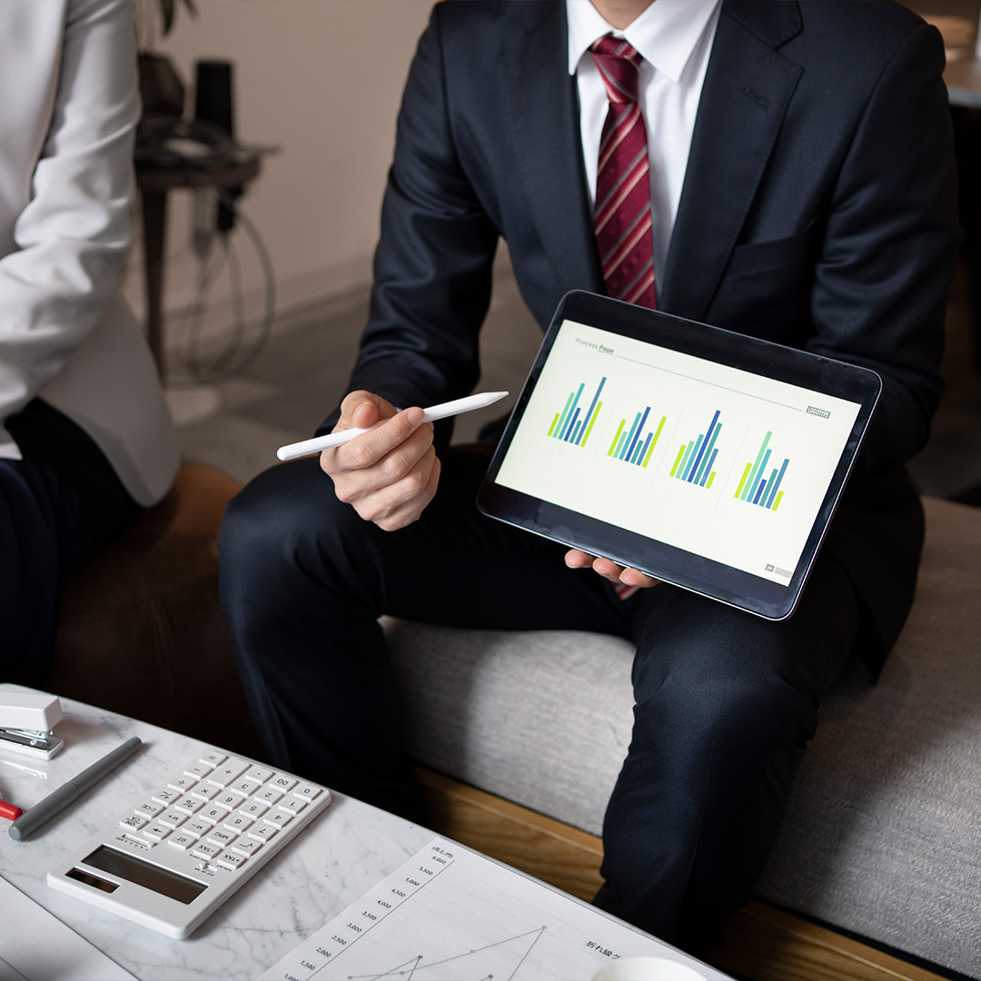 Business professional in a suit presenting performance charts on a tablet, with bar graphs indicating shareholder data and financial growth.