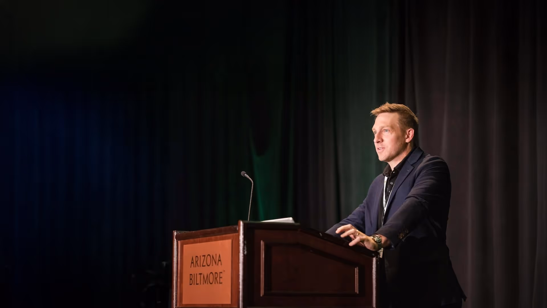 Nicholas Eggert speaking on stage at the Tenet Cup, delivering remarks from a podium at the Arizona Biltmore.