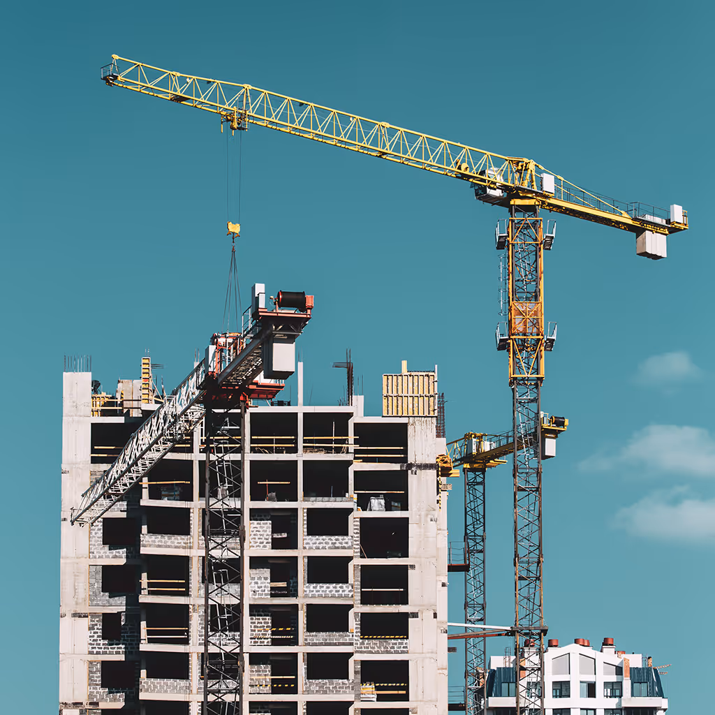 Yellow construction crane lifting materials over a multi-story building under construction against a clear blue sky.