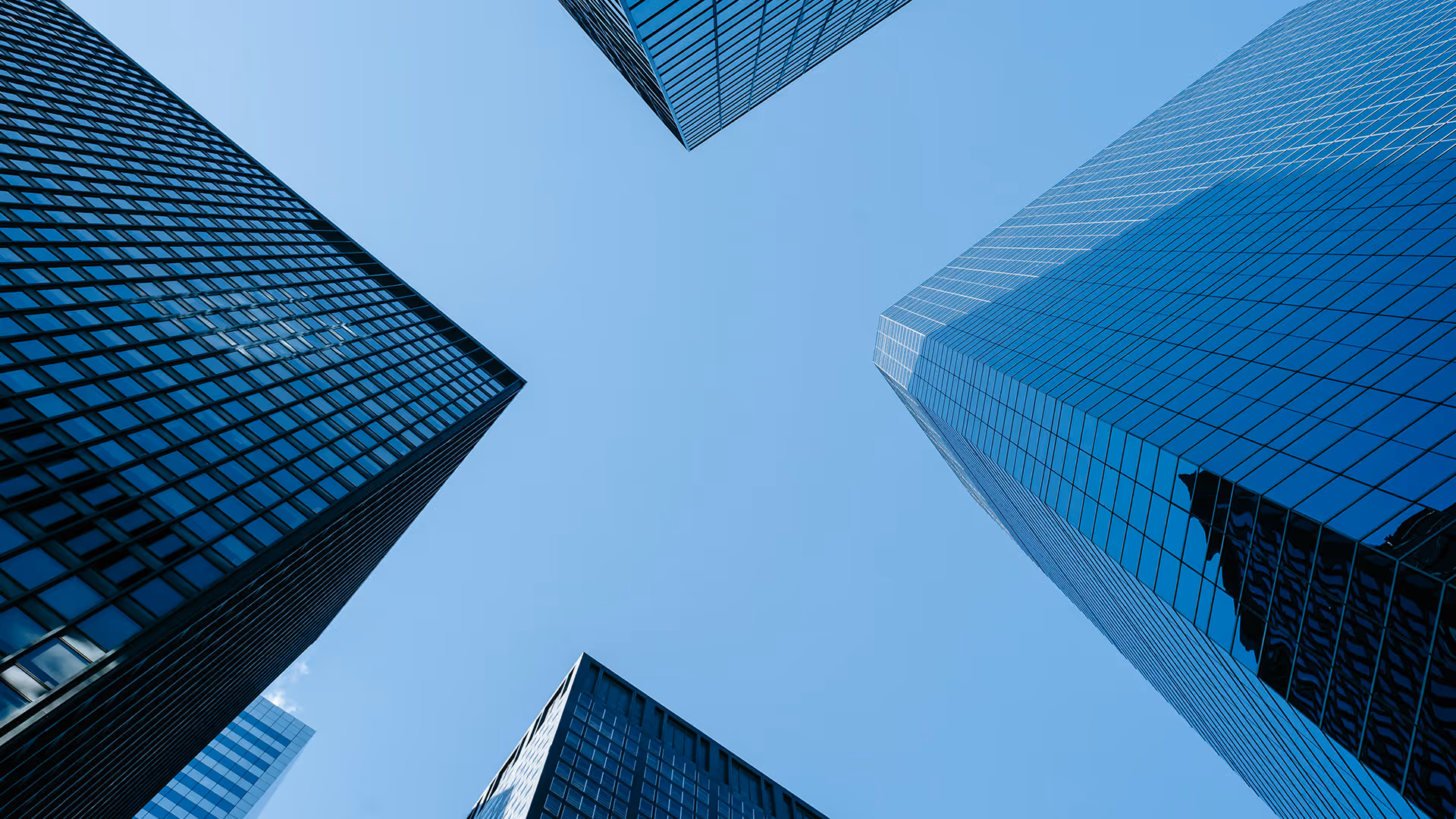Looking up at four modern glass skyscrapers against a clear blue sky.