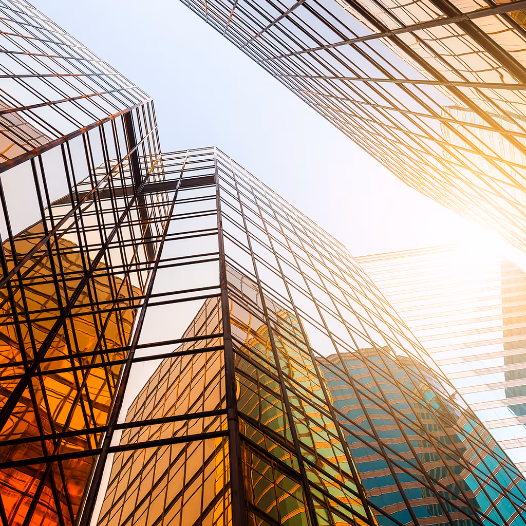 Upward view of modern glass skyscrapers reflecting sunlight and nearby buildings.
