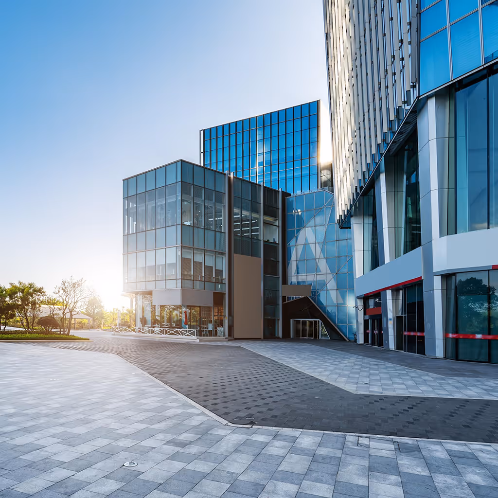 Modern glass office buildings with reflective blue windows and a paved walkway at sunrise.