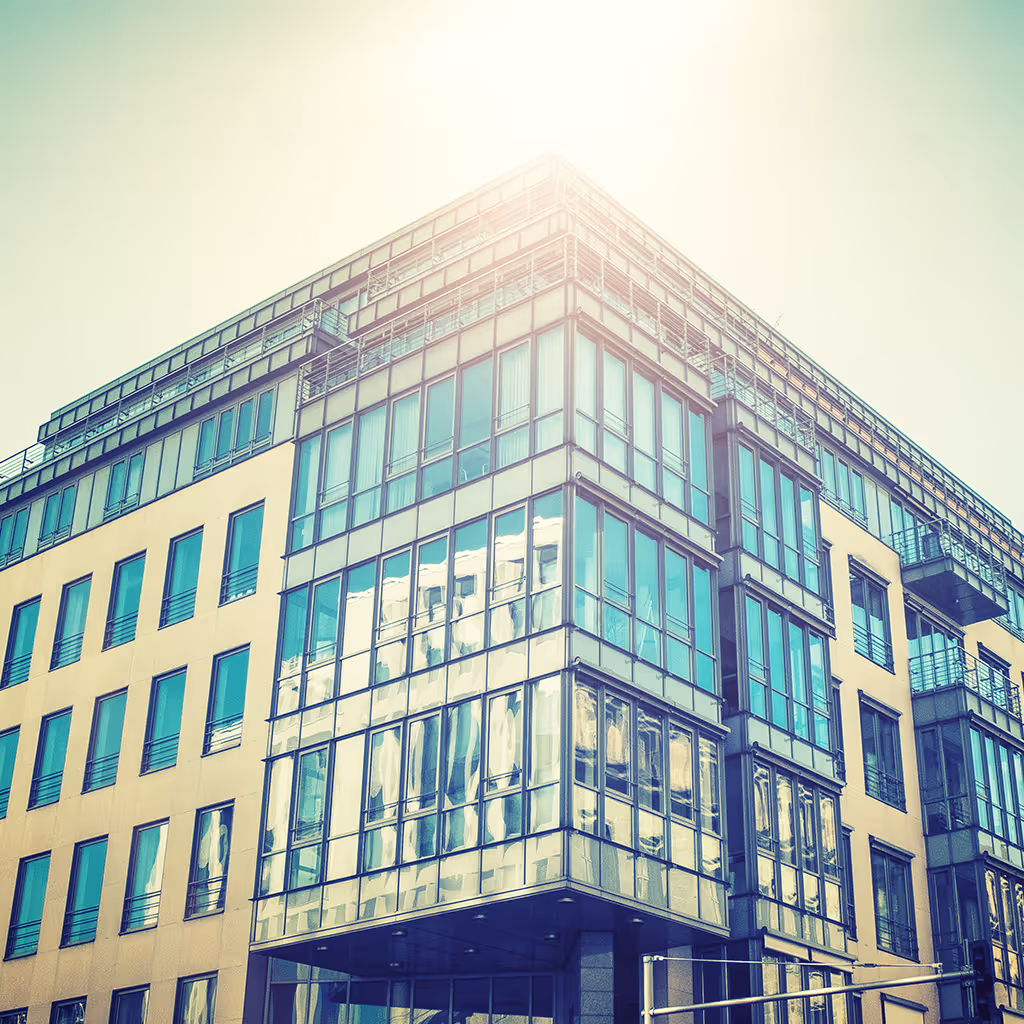 Modern office building with large reflective glass windows and upper floors under bright sunlight.